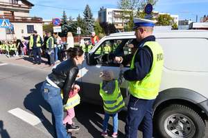 Policjant bierze udział w akcji Kierowco, proszę zwolnij. Przedszkolaki wręczają kierujacemu ulotki