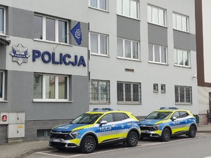 Dwa oznakowane radiowozy na tle Komendy Powiatowej Policji w  Dąbrowie Tarnowsakiej