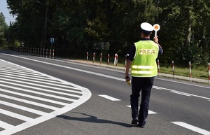 policjant ruchu drogowego w kamizelce odblaskowej na jezdni zatrzymuje pojazd
