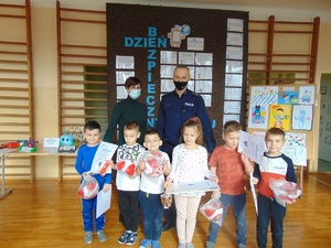 na zdjęciu grupa młodszych dzieci wspólnie z policjantem oraz nauczycielem. Dzieci trzymają dyplomy za udział w konkursie