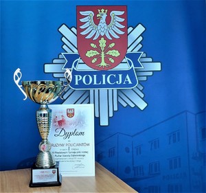 dyplom i puchar na tle logo Komendy Powiatowej Policji w Dąbrowie Tarnowskiej na niebieskim tle