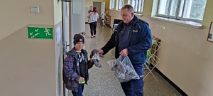 policjant wręcza dziecku misia na korytarzu w placówce tymczasowego pobytu