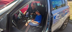 policjant siedzi na przednim siedzeniu pasażera a za kierownicą chłopczyk w czapce policyjnej