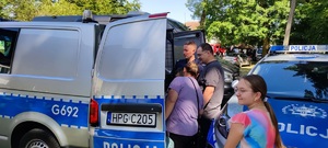 policjant prezentujący radiowóz oznakowany otwarte tylne drzwi a przy nim stojące osoby uczestniczące w pikniku