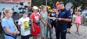 policjant prowadzący konkurs wiedzy o bezpieczeństwie stoi z mikrofonem w ręce a przed nim dzieci ustawione w rzędzie