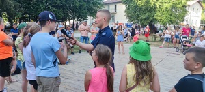 Policjant umundurowany prowadzi konkurs dla dzieci, trzyma w ręce mikrofon ia przed nim dzieci ustawione w rzędzie