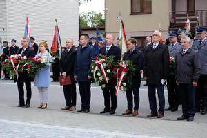 delegacje posłowie, władze miasta i gminy oraz inni przed pomnikiem z kwiatami w tle dom i tłum