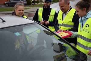 dzieci w kamizelkach odblaskowych, starosta powiatu i policjant wręczają kierowcy cytrynę