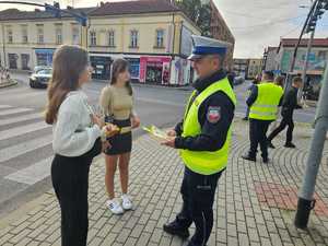 umundurowany policjant wręcza ulotki dwóm młodym kobietom