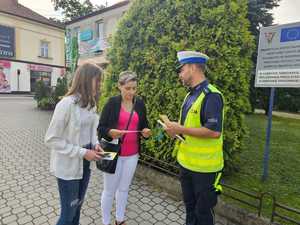 umundurowany policjant wręcza ulotkę przechodzącej kobiecie