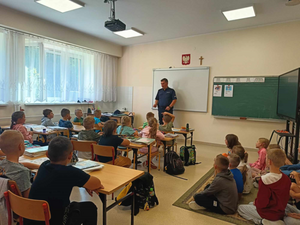 Policjant podczas przemówienia do dzieci przedszkolnych, szkolnych siedzących w ławkach